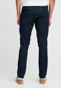 Mörkblå jeans med slim fit, utrustad med bakfickor och diskreta söm detaljer. Bärs med ljusa sneakers.