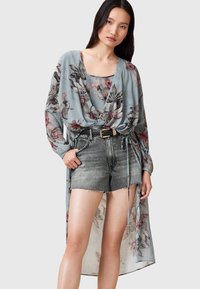 Top avvolgente azzurro chiaro traslucido con stampa floreale, abbinato a pantaloncini in denim grigio a vita alta. Maniche lunghe e dettaglio con laccio in vita.