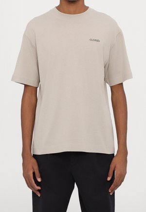 Vaaleanbeige lyhythihainen t-paita, joka on valmistettu puuvillasta. Paidassa on suora leikkaus ja sen etuosassa on mustalla kirjailtu sana "CLOSED".
