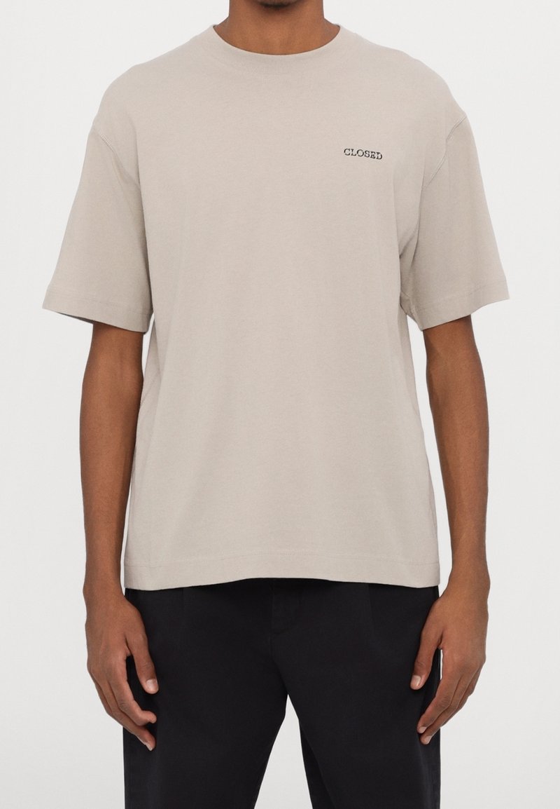 T-shirt beige clair à manches courtes en coton, avec une coupe droite et le mot "CLOSED" brodé en noir sur le devant.