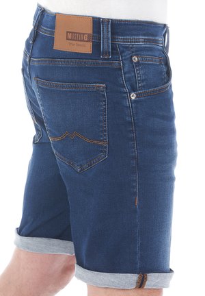Shorts en denim bleu foncé avec ourlets repliés, couture contrastante marron et une étiquette en cuir portant la mention "MUSTANG True Denim" sur la ceinture.
