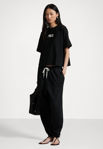 Tricou din bumbac negru cu logo-ul "POLO", asociat cu pantaloni de trening negri, de tip loose-fit, având un elastic cu șnur la talie și buzunare laterale.