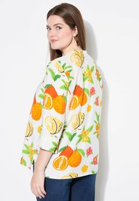 Hvid skjorte med lyse orange og gule citrusfrugtmønstre, grønne blade og blomsterdetaljer. Trekvartærmer, løs pasform.