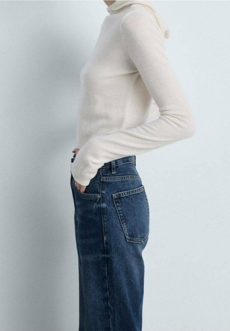 Suéter de cuello alto color crema hecho de material suave, combinado con jeans de mezclilla azul de cintura alta que presentan un detalle en el bolsillo trasero y un corte recto clásico.