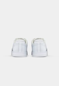 Adidași din piele albă cu design low-top, având o suprafață texturată și accente negre contrastante pe laterale. Tălpi plate din cauciuc.