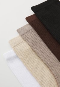 Set of five ribbed socks in varying colors: white, beige, light brown, dark brown, and black. Made of soft knit fabric with elastic cuffs.