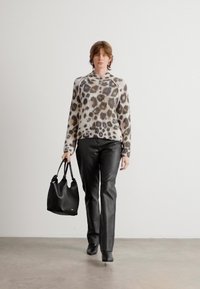 Pull en imprimé léopard avec texture côtelée, associé à un pantalon en cuir noir et un sac tote noir, présentant un design simple et une finition lisse.