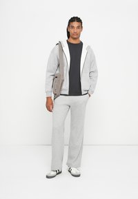 Szürke kapucnis pulóver fehér béléssel, fekete póló és hozzáillő szürke melegítőnadrág. Egyszerű dizájn, textúrált anyag, lazás stílus. Fekete-fehér sportcipők.