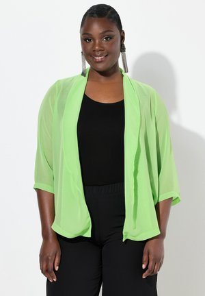 Leggero kimono verde lime trasparente con maniche ampie, design a strati, indossato sopra una maglietta nera e pantaloni neri.