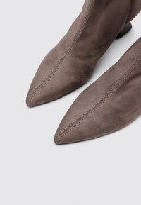 Bottines en suede gris avec des bouts pointus, présentant des détails cousus le long des coutures et un talon bloc bas. Texture lisse.