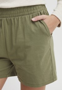 Olivgröna bomullsshorts med elastisk midja och sidofickor, med en slät textur och enkel skärning för komfort.