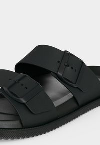 Sandale slide noire avec deux sangles réglables à boucles et semelle texturée.
