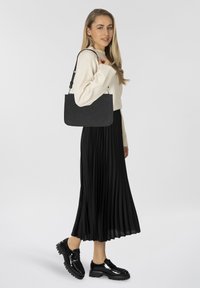 Borsa a mano nera in pelle con tracolla sottile, caratterizzata da una texture liscia e una forma rettangolare. Indossata con una gonna nera plissettata e scarpe nere lucide.