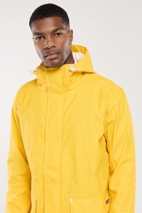 Veste imperméable jaune avec un col montant et une capuche à cordon de serrage. Dotée de poches avant et d'une texture lisse et brillante.