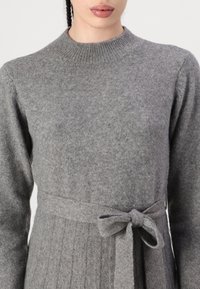 Abito grigio a maglia con corpino attillato e gonna svasata. Presenta un colletto rotondo, maniche lunghe e una cintura in tessuto legata in vita.