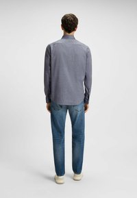 Donkergrijze heren overhemd met lange mouwen en subtiele ruitjespatroon, gecombineerd met lichtblauwe denimjeans en witte sneakers.