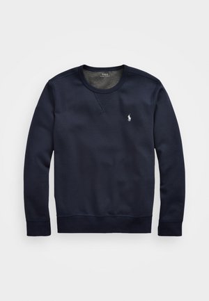 Mørkeblå genser med lange ermer, rund hals og ribbestrikkede mansjetter. Har en liten hvit logo på venstre bryst og en jevn stofftekstur.