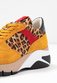 Sneaker med leopardmönstrad ovandel i gult mocka och röda accenter. Tjock sula med vita och svarta inslag. Snörning i matchande färg.