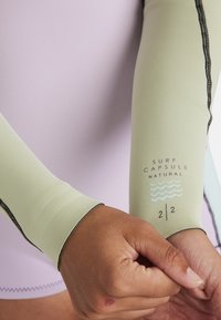 Maniche per surf di colore verde chiaro realizzate in materiale elastico, con cuciture nere e un logo stampato con grafiche di onde.