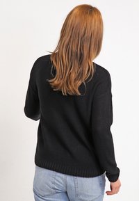 Černý pletený svetr s volnějším střihem, žebrovaným lemem a manžetami a texturovaným vzorem. Nositelný s světle modrými džíny, které zdůrazňují ležérní styl.