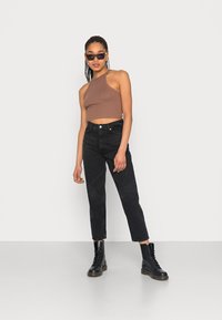 Top cropped halterneck em malha castanha combinado com jeans pretos de cintura alta e botas pretas com atacadores. Design minimalista, silhueta justa e tecido texturizado.