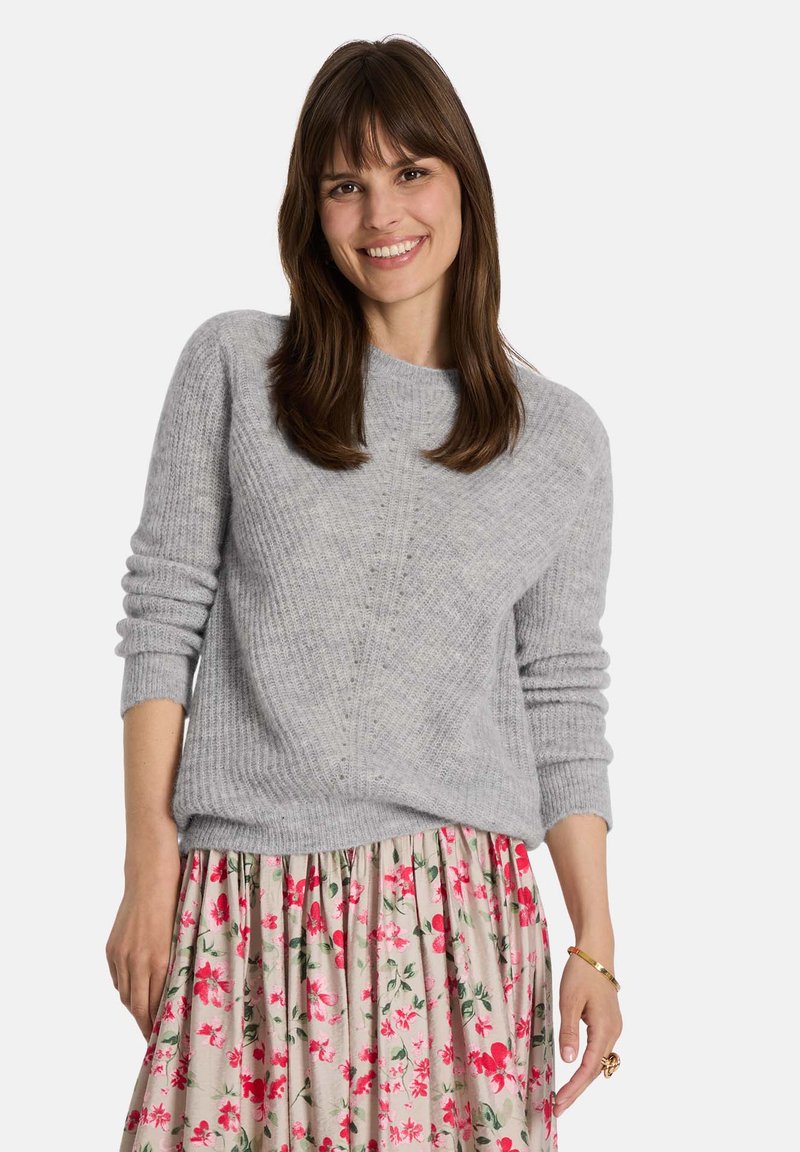 Grauer Strickpullover mit Rundhalsausschnitt und gerippter Struktur, kombiniert mit einem rock mit Blumenmuster in Pink, der weichen Stoff und lässiges Design zeigt.