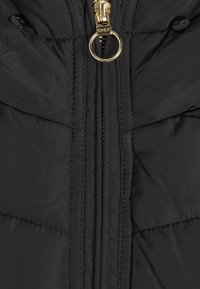 Sort puffermantel tæt på, med en gullig lynlås med ringtræk, knapdetaljer og quiltet tekstur med kontrasterende syninger.