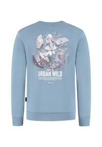 Lichtblauwe sweatshirt met een ontwerp van een witte bloem die door grijze betonnen scherven breekt, met de tekst "URBAN WILD" eronder.