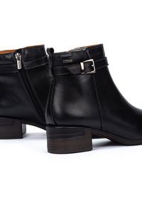 Botas de tobillo de cuero negro con cremallera lateral, una hebilla decorativa y un tacón de madera marrón. Textura suave con costuras reforzadas.