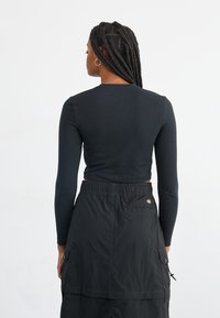 Fekete, hosszú ujjú crop top, amelyet egy fekete, térd alá érő cargo szoknyával párosítottak, zsebekkel és elasztikus derékrésszel.