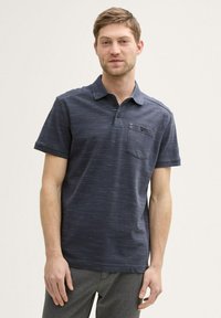 Niebieska koszulka polo w kolorze granatowym z subtelnym wzorem teksturalnym, zapięcie na trzy guziki i kieszonką na piersi. Krótkie rękawy i luźny krój.