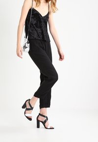 Camisola in velluto nero con spalline sottili, abbinata a pantaloni neri larghi. Le calzature presentano tacchi a cinghie bianchi e neri.