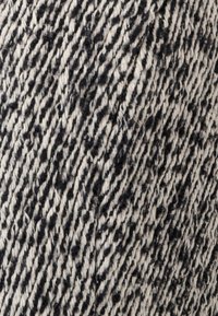 Textile avec un motif texturé en noir et crème. Le matériau semble tissé avec des fibres visibles créant un design rayé.