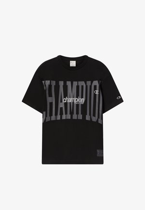 Camiseta negra de Champion con el gran texto gris "CHAMPION" y el logo más pequeño en blanco "champion NEW YORK" en el pecho, y el logo "C" de Champion en la manga.