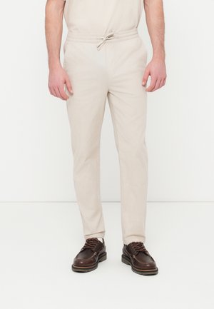 Pantaloni intrecciati color beige chiaro con vita elastica regolabile con coulisse, tasche laterali e taglio a gamba dritta, abbinati a scarpe marrone scuro.