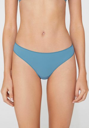 Mujer con braguitas de bikini azul claro, mostrada desde la mitad del torso hasta la parte superior de los muslos sobre un fondo liso.