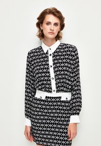 Black and white patterned dress with a pointed collar, long sleeves, a white belt, and button details on the front and cuffs.