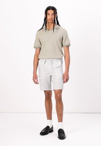 Lys grå shorts med et teksturert stoff, parret med en salviegrønn kortermet polo, og svarte loafers med hvite sokker.