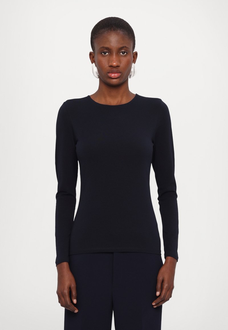 Navy long-sleeve top made from a smooth, fitted fabric. Features a round neckline and tapered sleeves, worn with matching dark pants.