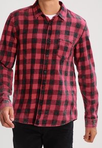 Rood en zwart geruit flanellen shirt met lange mouwen, knoopsluiting aan de voorkant en een enkele borstzak. Zachte textuur en afgeronde zoom.