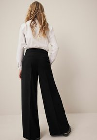 Schwarze weit geschnittene Hose aus einem glatten Stoff, mit hoher Taille, zwei Gesäßtaschen und tailliertem Schnitt.