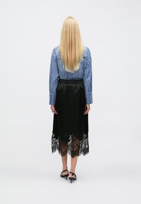 Blauw-wit gestreept overhemd met lange mouwen, gecombineerd met een zwarte satijnen rok met een kanten rand aan de zoom. Zwarte schoenen met dunne hak.