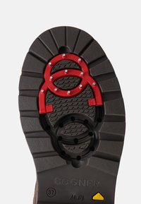 Czarna gumowa podeszwa z teksturowanym wzorem antypoślizgowym, z czerwonymi akcentami i okrągłymi elementami. Zawiera szczegóły dotyczące marki i rozmiaru.