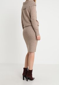 Robe-pull en laine beige douce avec un col bénitier plié, coupe ajustée, texture côtelée, associée à des bottines bordeaux.