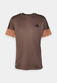Camiseta atlética marrón de manga corta con mangas contrastantes en naranja claro. Presenta un logo negro y rayas horizontales negras en los hombros.