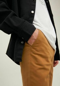 Black corduroy jacket with snap buttons over a white shirt, paired with tan cotton pants, showcasing a relaxed fit and smooth texture.
