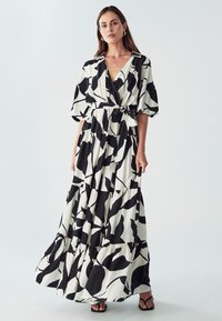 Maksistruk u crno-bijeloj boji, s uzorkom lista, V-izrezom, kratkim rukavima, vezanim strukom i višeslojnim suknjom s lepršavom teksturom.