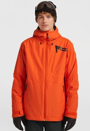 Feloranjeski-jas met een ritsborstzak, verstelbare capuchon en zwarte accenten, gecombineerd met donkere handschoenen en een beanie.
