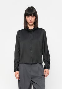 Blusa de satin preta com fecho de botão na frente, colarinho pequeno e mangas longas; textura suave com botões brilhantes e um ajuste confortável.
