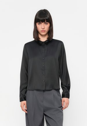 Black satin blouse with a button-down front, a small collar, and long sleeves; smooth texture with shiny buttons and a relaxed fit.